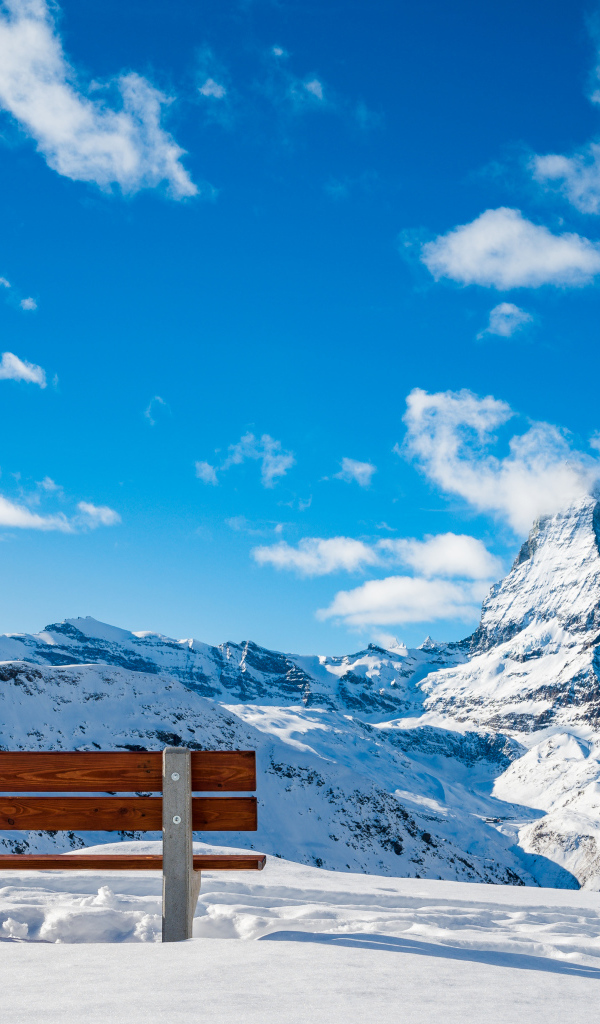 Лавка в заснеженных горах под голубым ясным небом