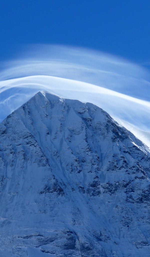 Белое облако в голубом небе над заснеженной горной вершиной