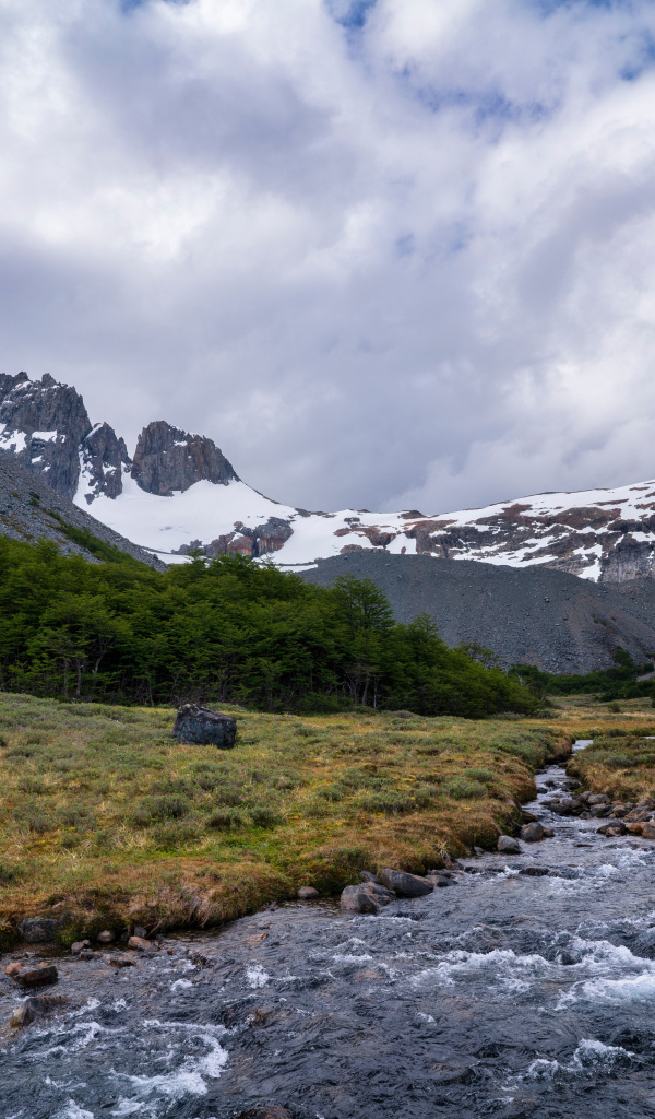 Быстрая река у заснеженных гор под густыми белыми облаками