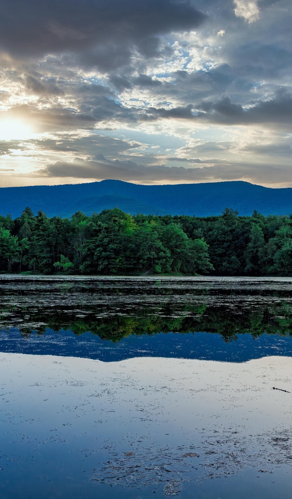 Солнце пробивается сквозь облака в небе над озером