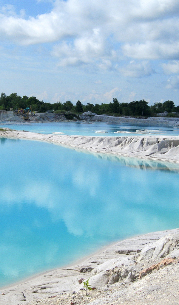 Белый песок на берегу водоема с голубой водой 