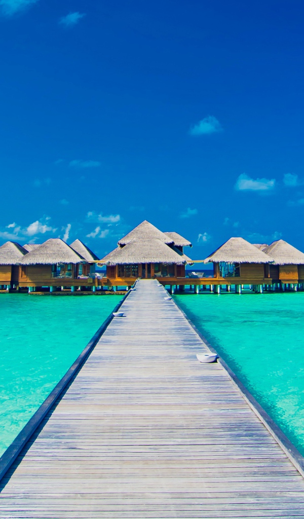 Деревянный мост к домам на сваях в голубом океане 