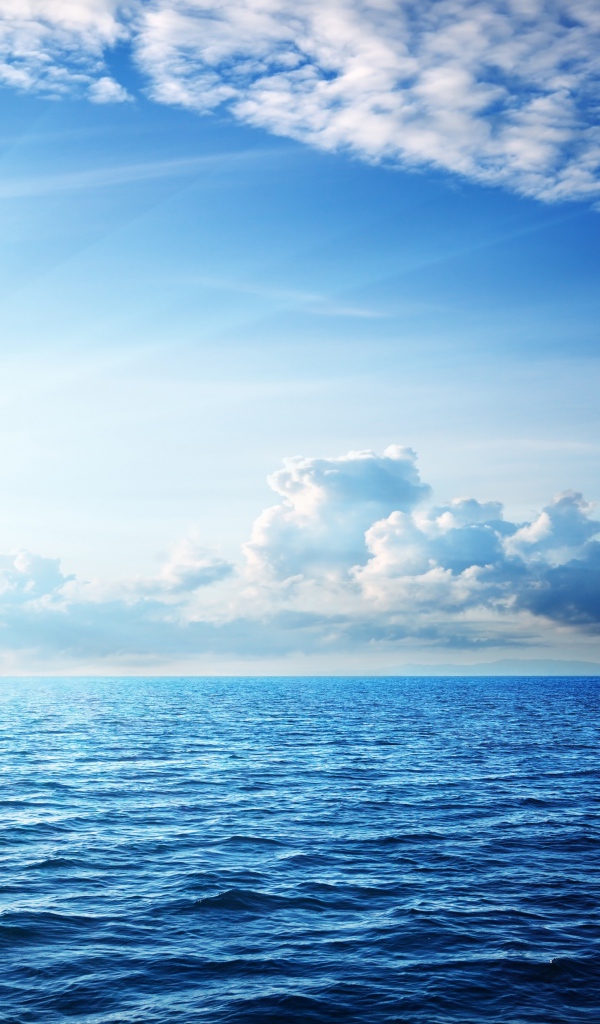 Спокойное синее море под ясным небом с белыми облаками
