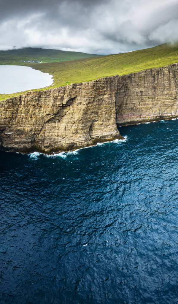 Океан омывает зеленый утес под пасмурным небом