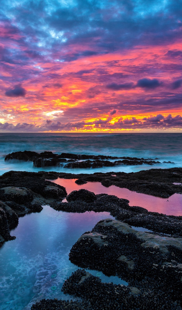 Восход яркого солнца над камнями в море