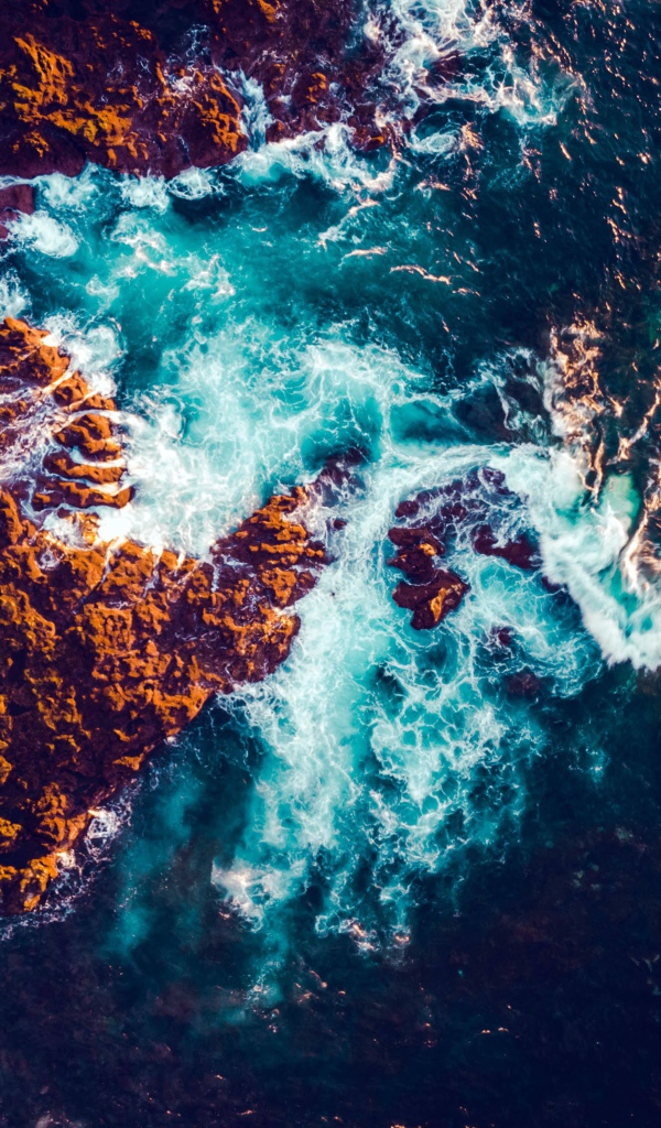 Белые морские волны бьются об камни, вид сверху