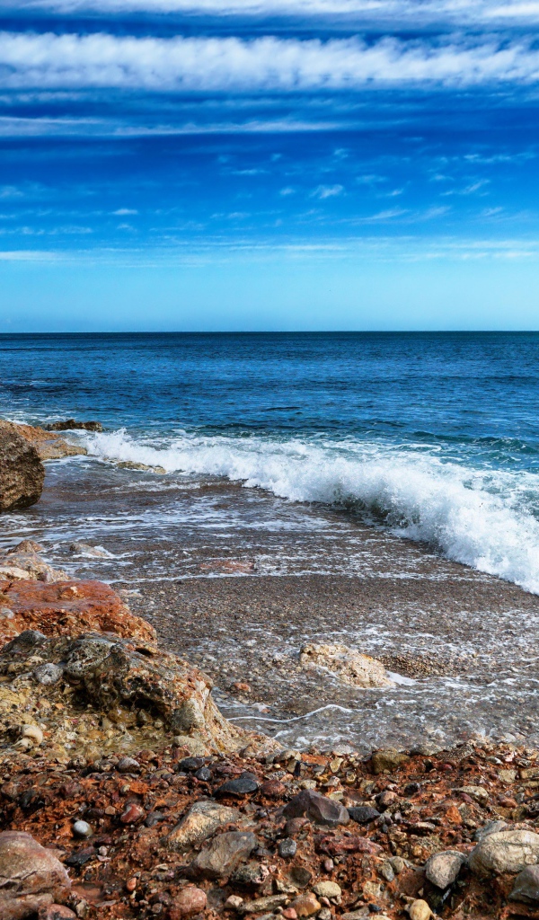 Белые волны на берегу моря с большими камнями под голубым небом