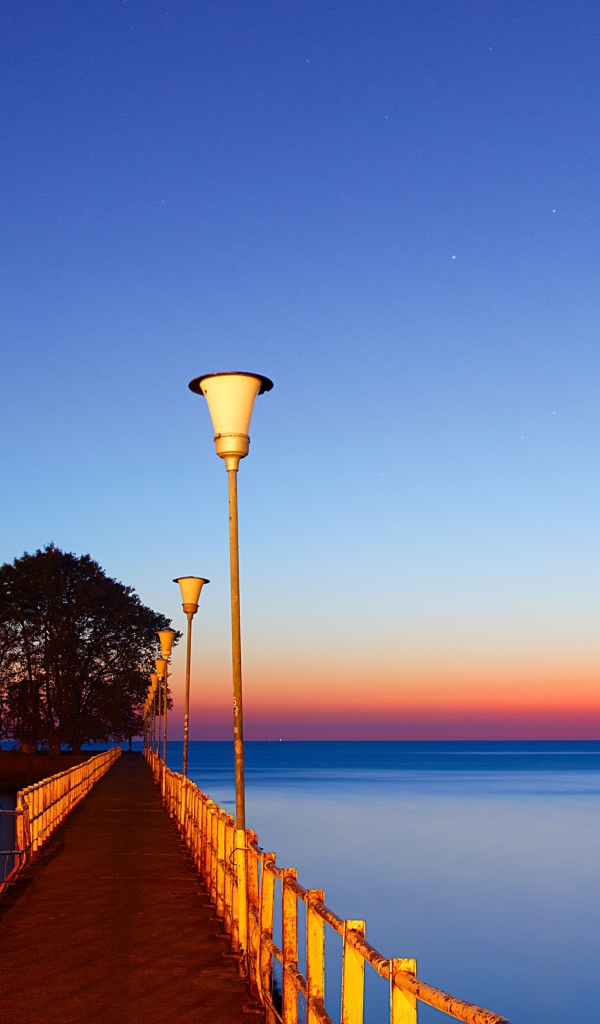 Мост в фонарями в море на закате 