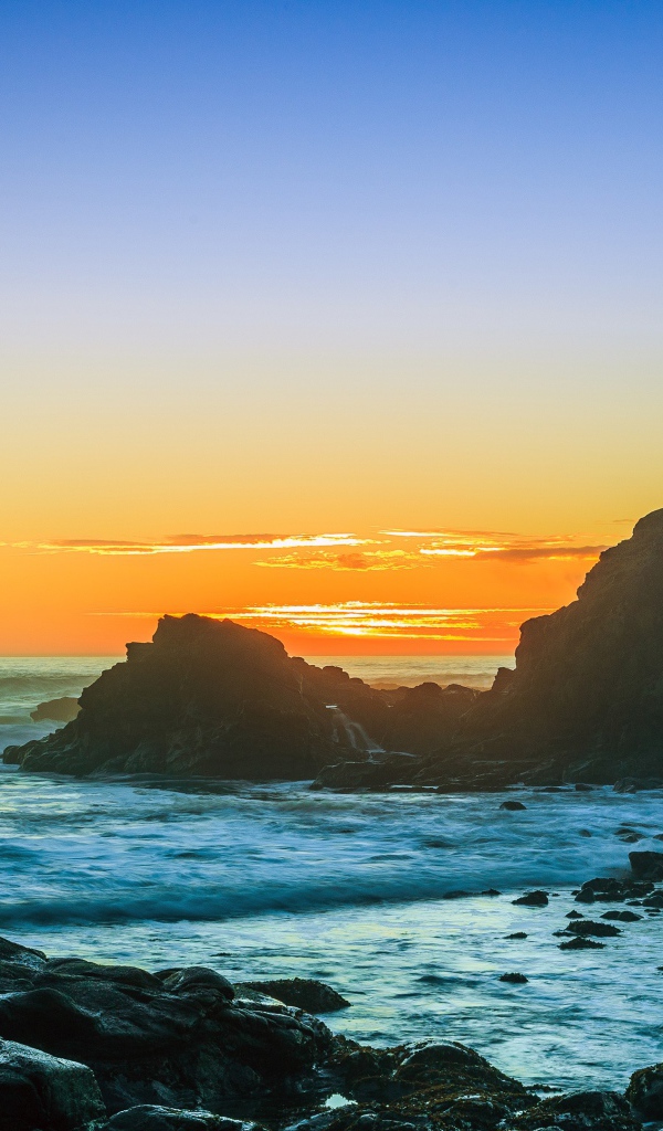Закат солнца над океаном с камнями на берегу 