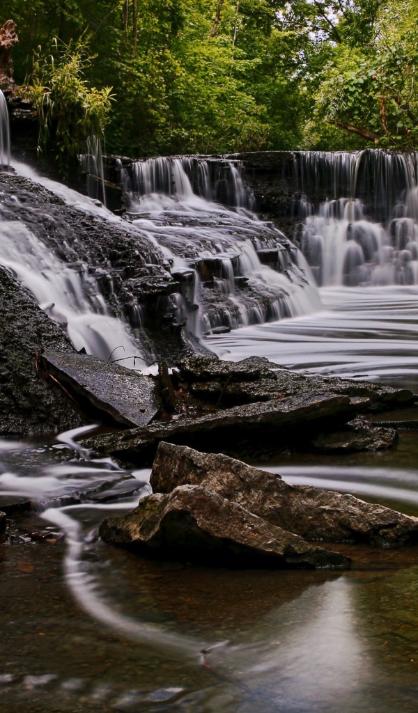 Быстрая вода стекает по камням водопада в парке 