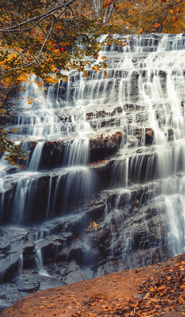Быстрая вода водопада стекает по каскадам камней осенью