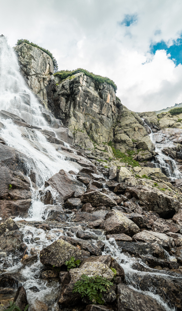 Водопад стекает по камням на фоне неба с белыми облаками