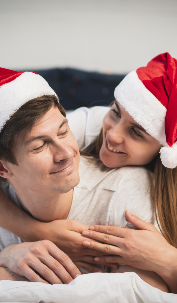 Мужчина и девушка в шапках Санта Клауса лежат на кровати 