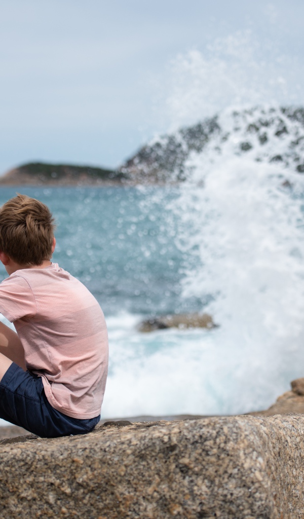 Мальчик сидит на камнях у бушующего моря