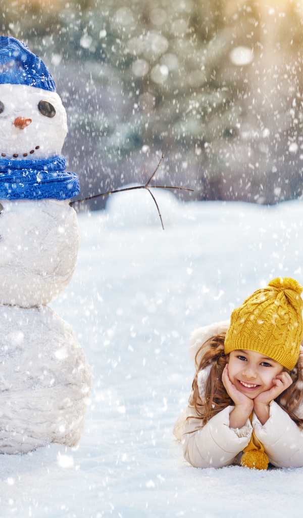 Милая девочка лежит на снегу у снеговика зимой
