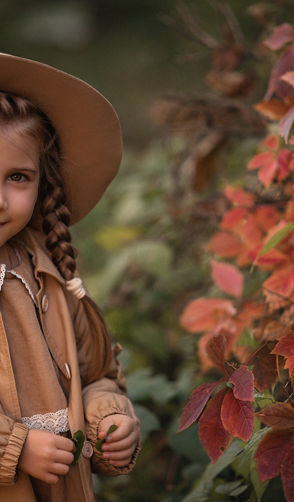 Красивая девочка шляпе стоит у дикого винограда 