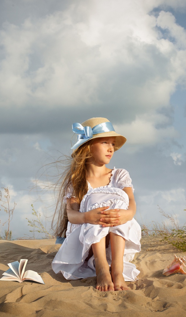 Красивая девочка в белом платье сидит на песку