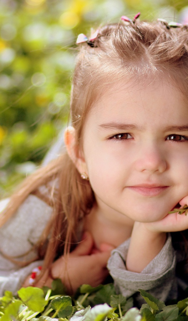 Красивая маленькая кареглазая девочка лежит на траве 