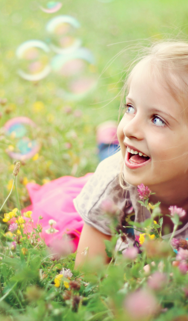 Веселая девочка лежит на траве с мыльными пузырями