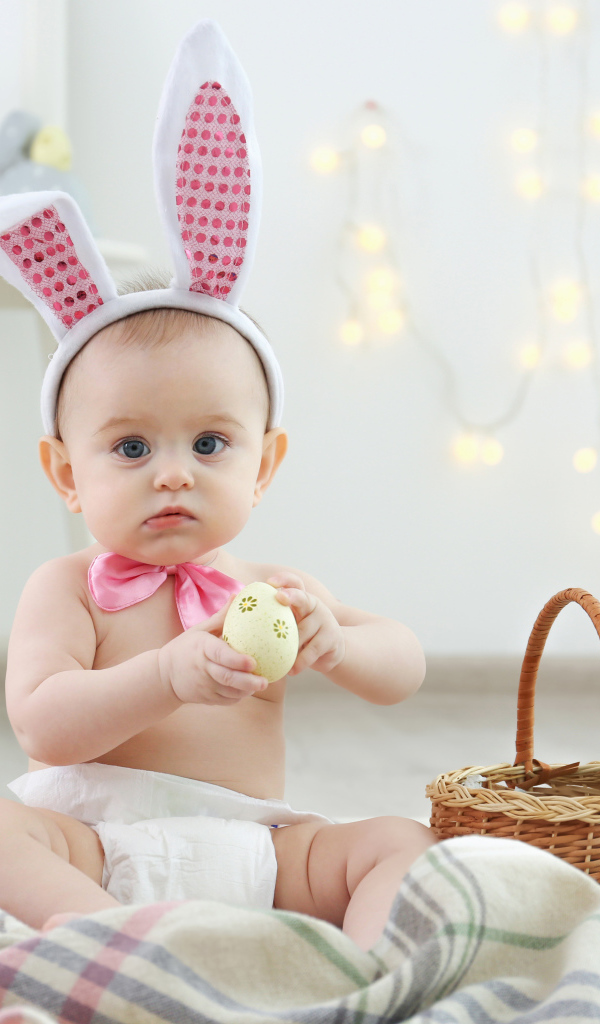 Милый ребенок с ушками на голове сидит пасхальными яйцами