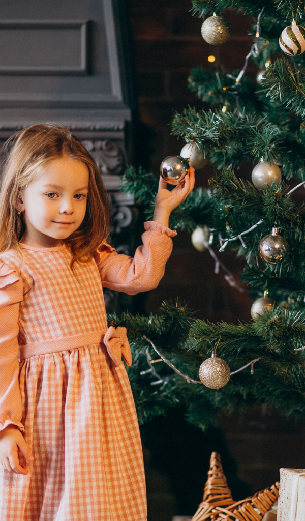 Милая маленькая девочка стоит у наряженной елки 