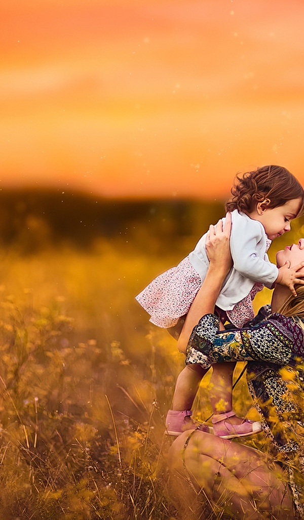 Девушка держит маленькую девочку на руках в поле на закате