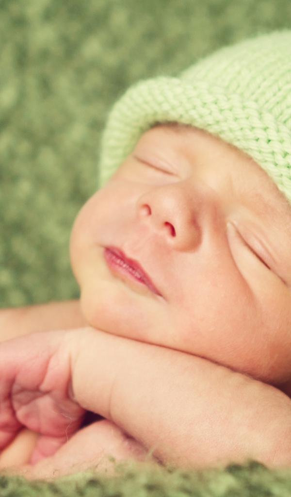 Зеленая вязаная шапка на голове у спящего ребенка 