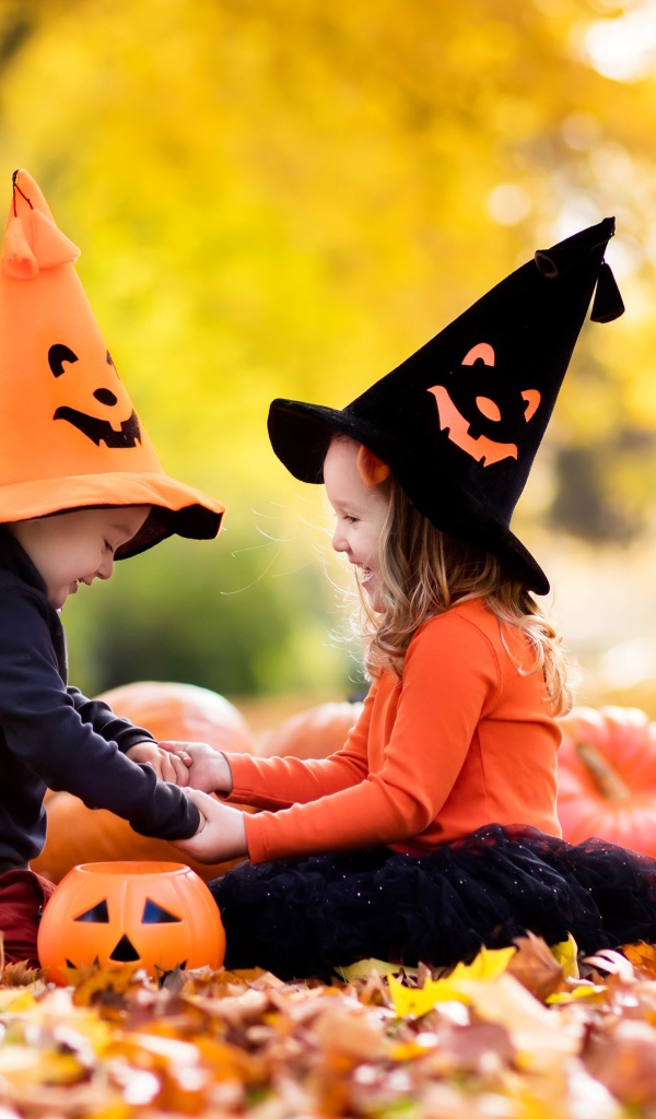 Маленькие мальчик и девочка в костюмах на Хэллоуин сидят на листве