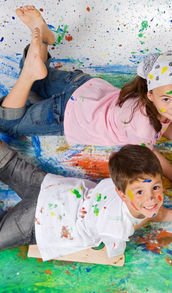 Маленькие мальчик и девочка рисуют красками на полу 