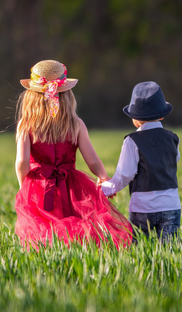 Маленькие мальчик и девочка идут по зеленому полю