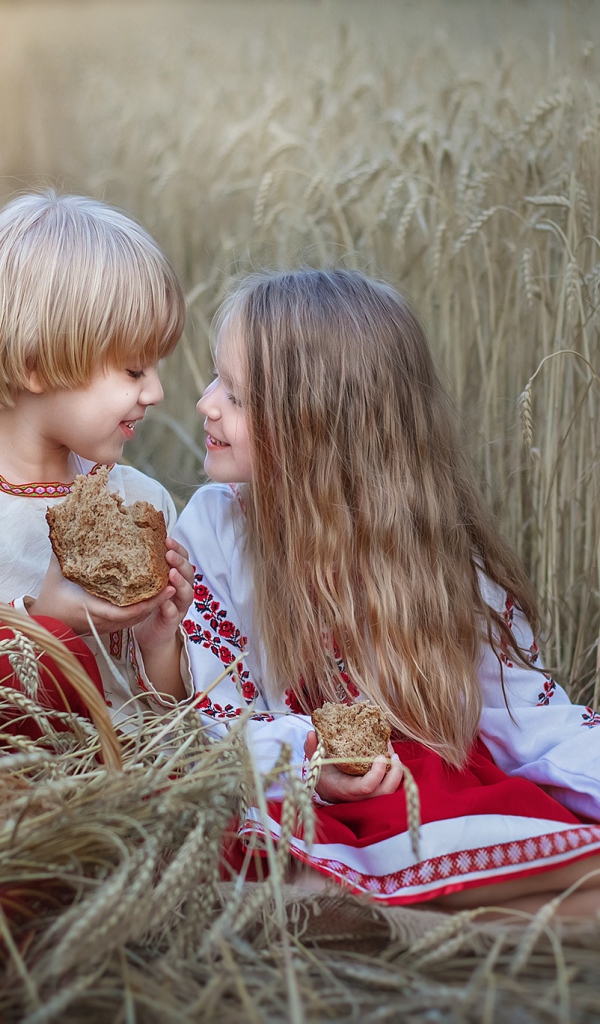 Маленькие мальчик и девочка с хлебом на пшеничном поле 