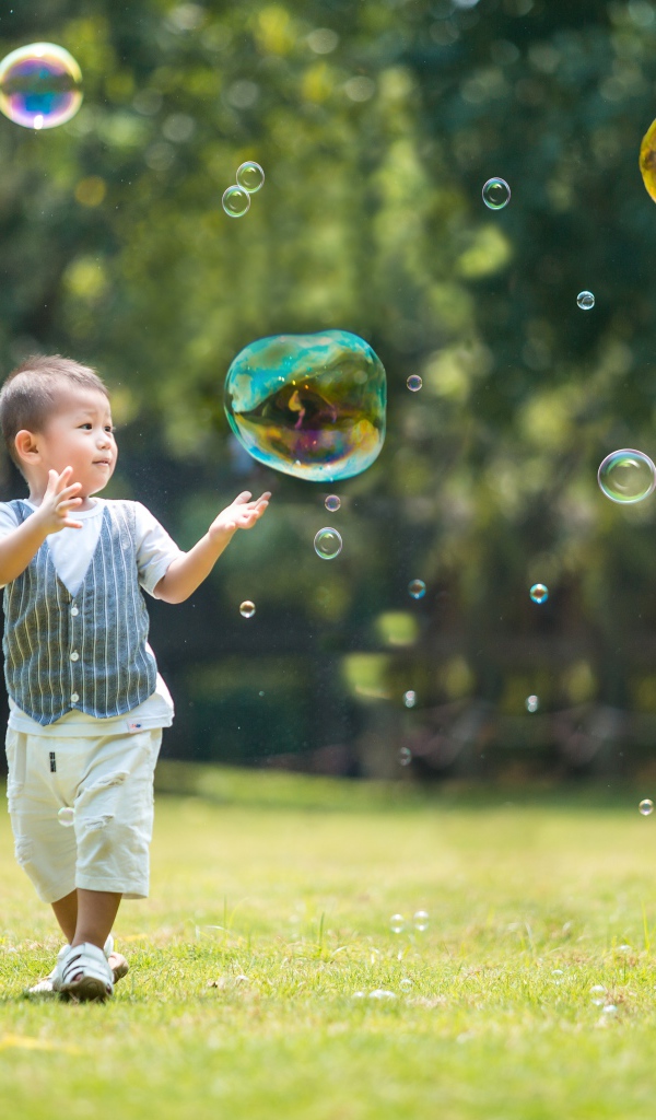 Маленький мальчик ловит мыльные пузыри
