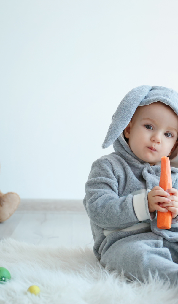 Маленький мальчик в костюме зайчика грызет морковь