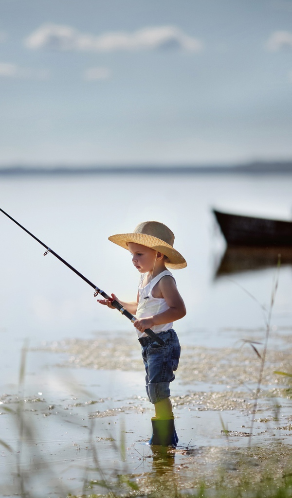 Маленький мальчик в шляпе ловит рыбу в озере 
