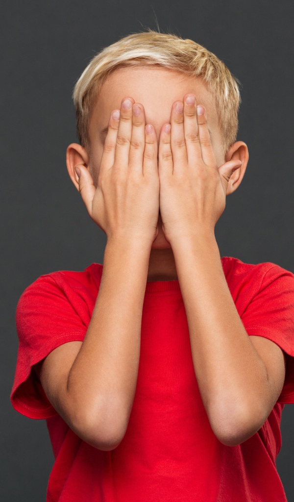 Маленький мальчик в красной футболке закрыл лицо руками 