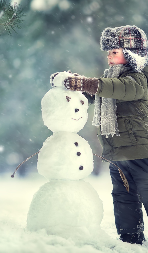 Маленький мальчик лепит снеговика зимой