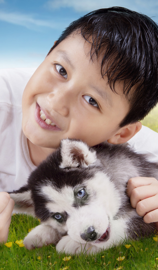 Маленький мальчик с щенком хаски на зеленой траве