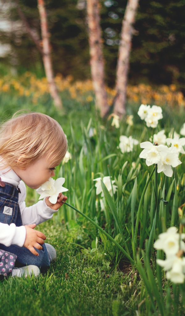 Маленький ребенок сидит на земле с нарциссами