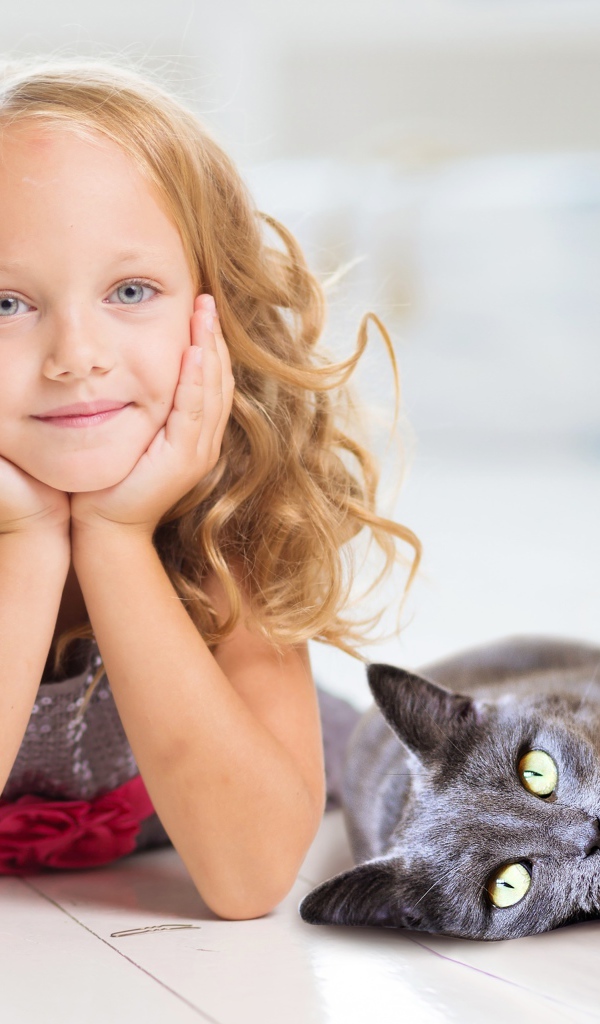 Маленькая милая голубоглазая девочка лежит на полу с котом