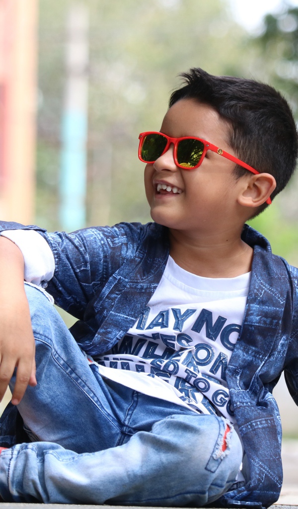 Маленький модный мальчик сидит на асфальте