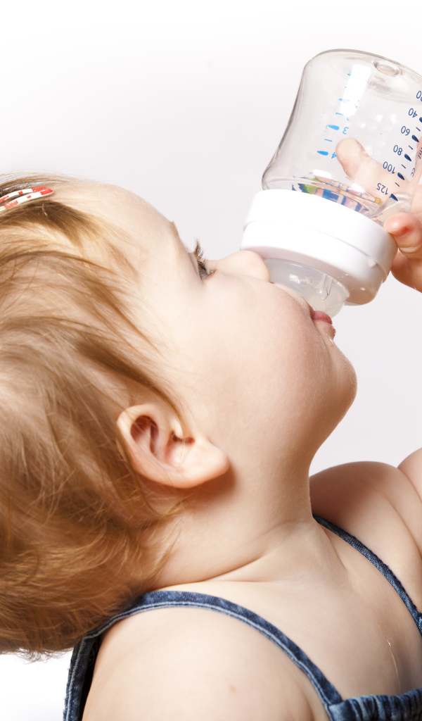 Маленькая девочка пьет молоко с бутылочки на белом фоне