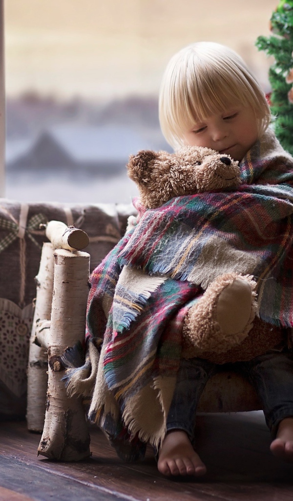 Маленькая девочка обнимает мишку у ели