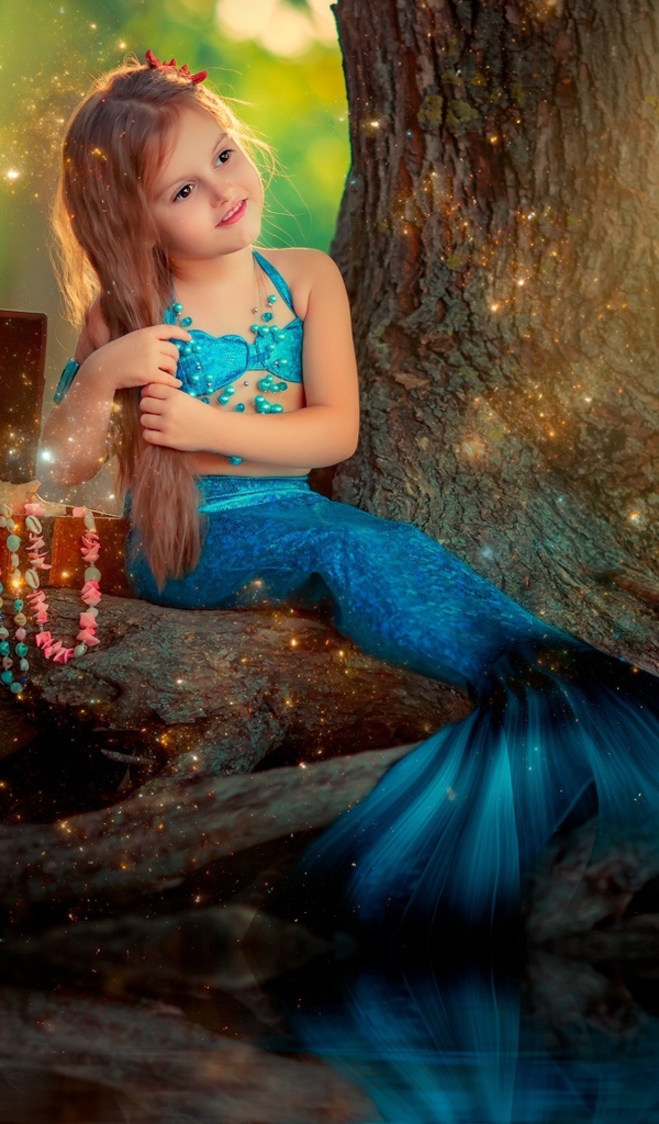 Маленькая девочка в костюме русалочки сидит у воды 