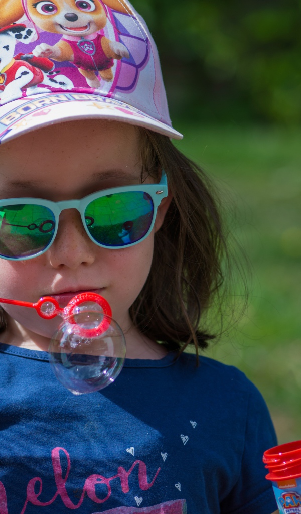 Маленькая девочка в очках с мыльными пузырями