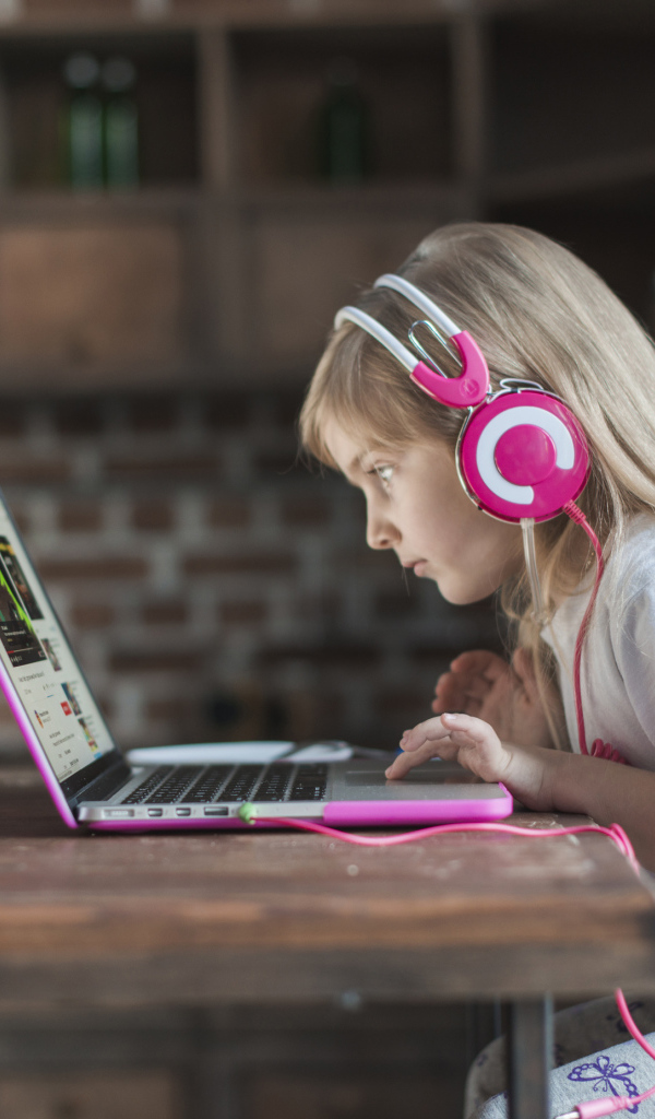 Маленькая девочка в наушниках сидит за ноутбуком
