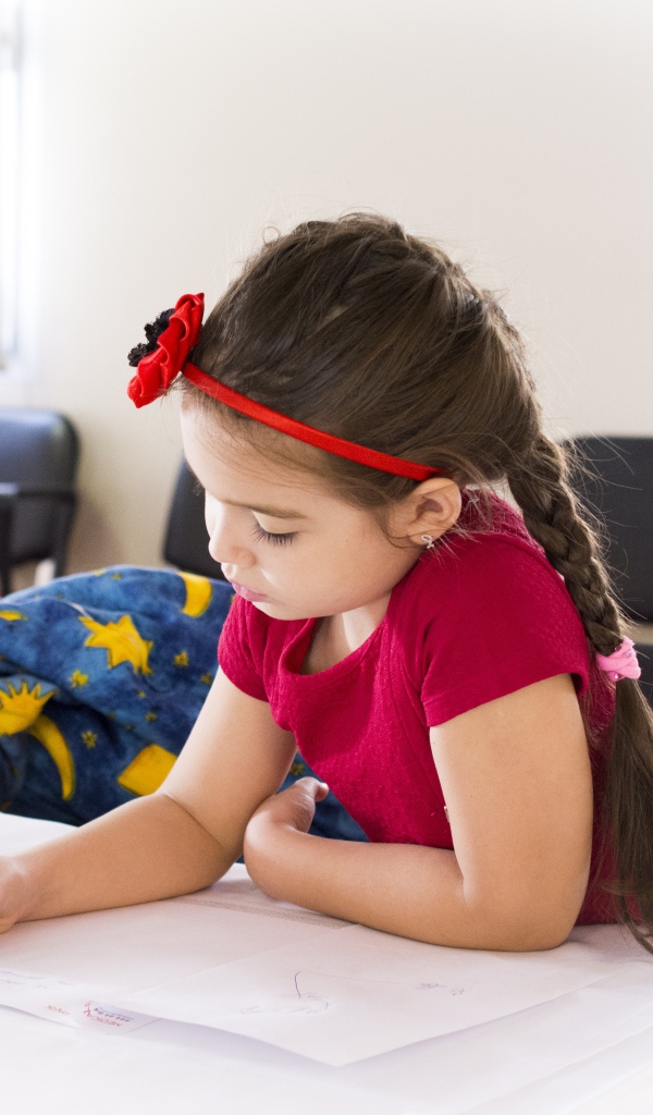 Маленькая девочка в красном платье рисует за столом