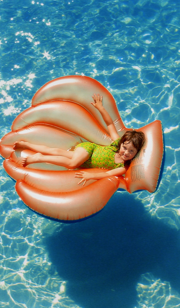 Маленькая девочка на надувном матрасе в бассейне летом 