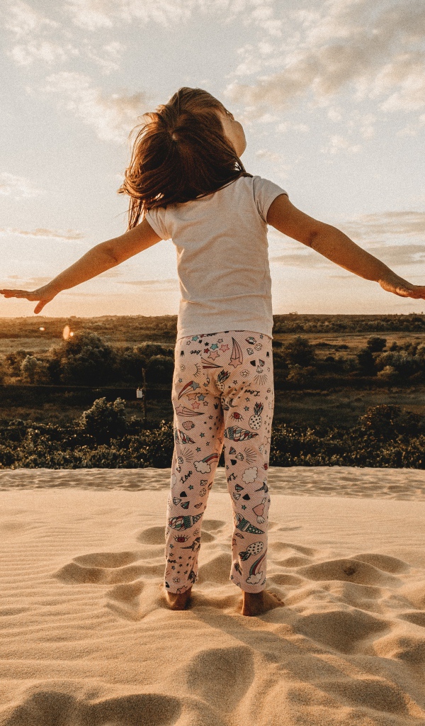 Маленькая девочка стоит на песку в лучах солнца