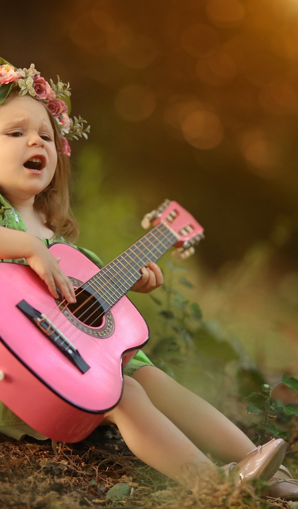 Маленькая девочка с гитарой под деревом 