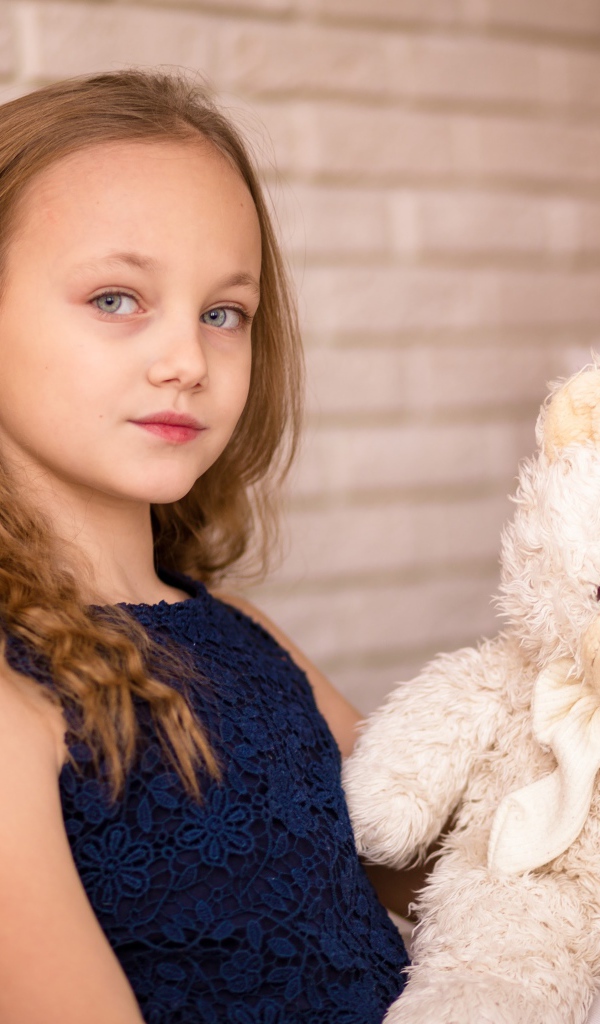 Маленькая девочка с мишкой сидит у наряженной ели 